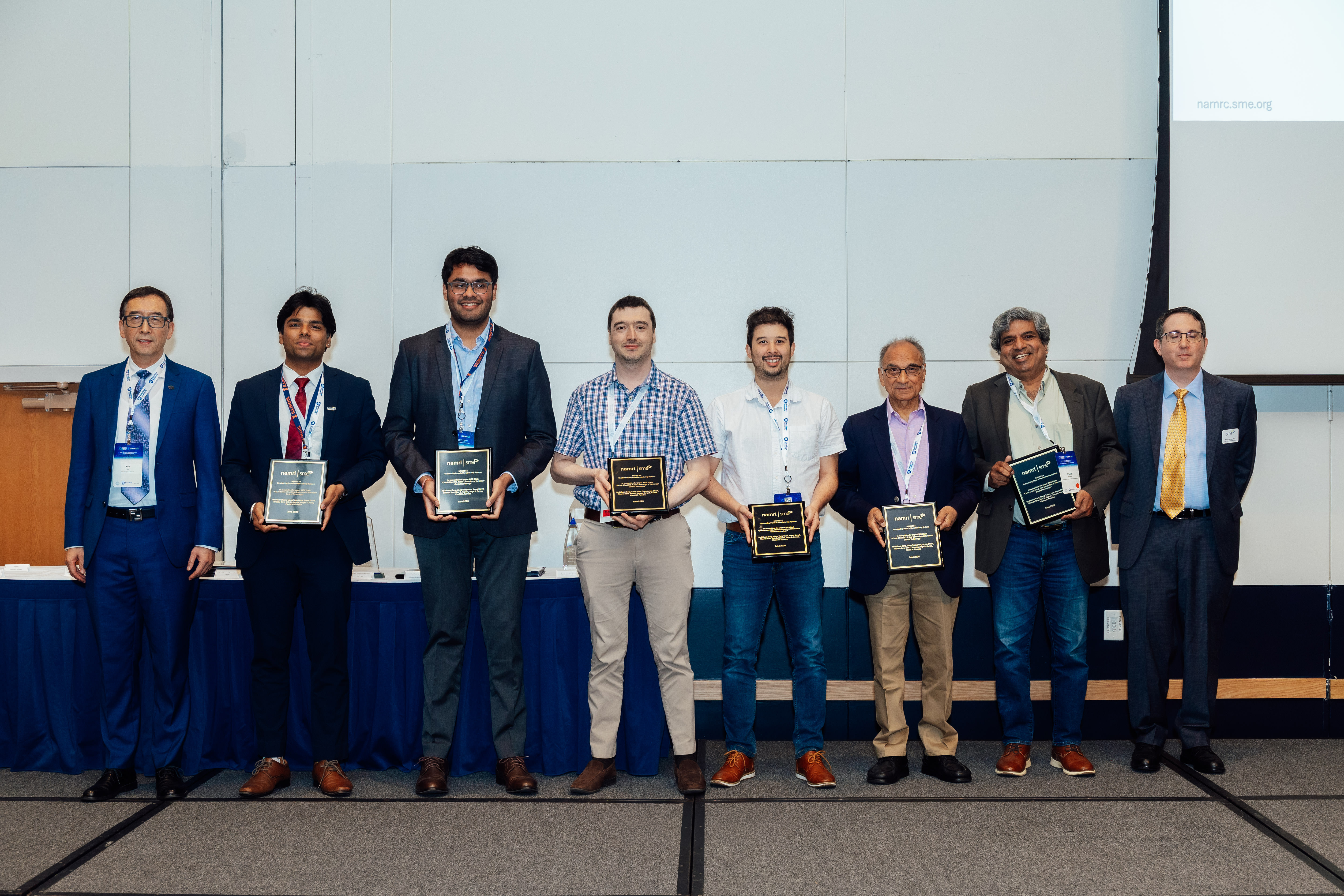 Six of the seven authors accept their NAMRC Outstanding Paper award on June 17, 2026. At the far left and far right are conference officials Xun Xu and Brett Conner. Holding the plaques are (left to right) authors Shivam Garg, Aryan Shroff, Ricardo Toro, Jorge E. Correa, Shiv G. Kapoor, and Placid M. Ferreira. Co-author Liang Tung Chen was not present.