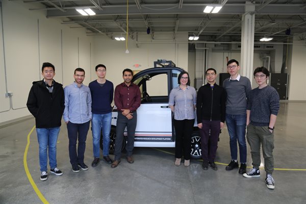 A group of staff and students in front of a smart car in the CSL High Bay.