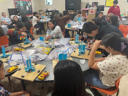 Photo shows children working on projects while sitting at a round table.